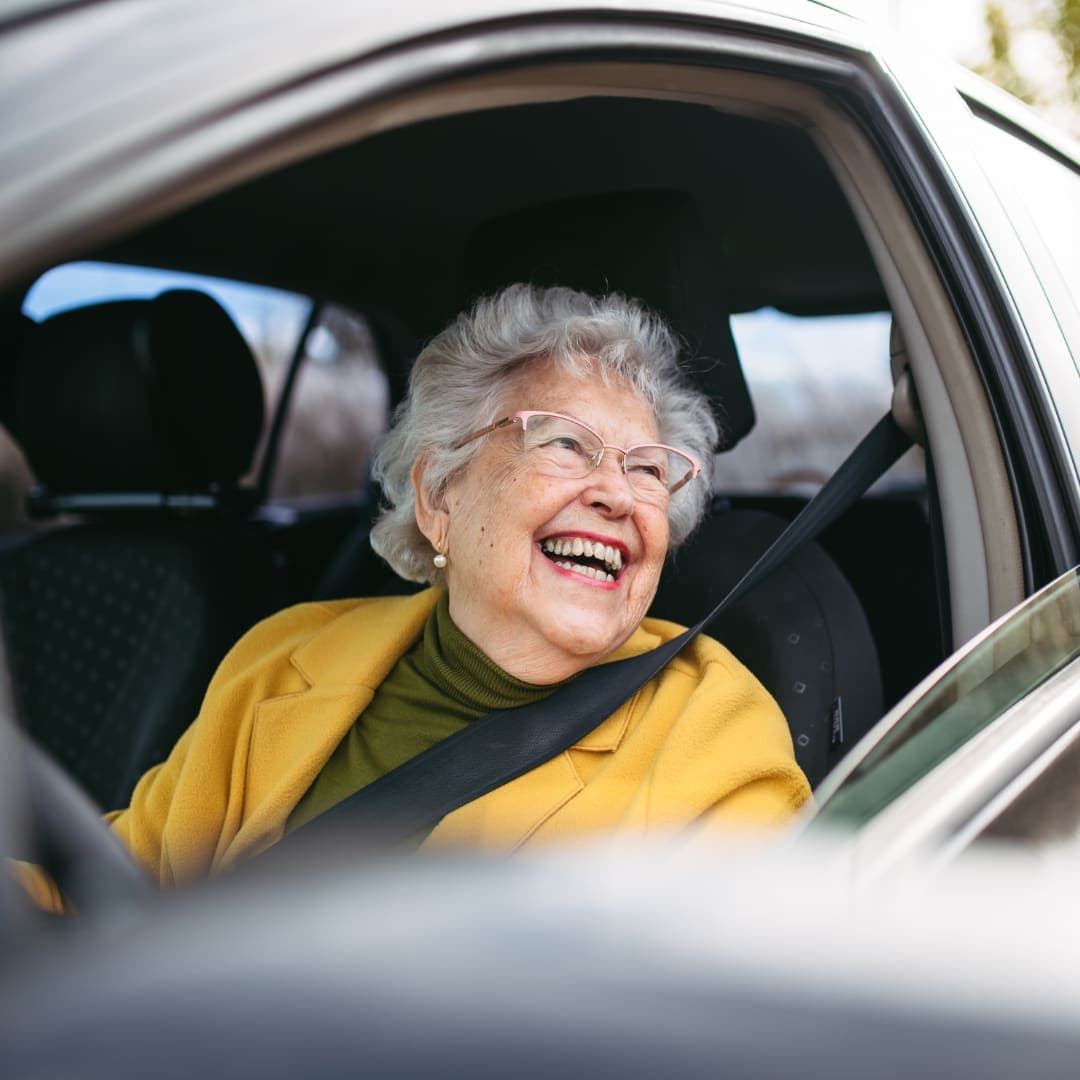 A smiling older woman in the passenger seat with her seatbelt on